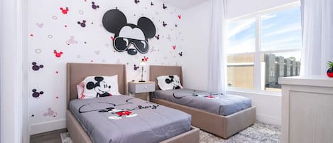 Habitación de hotel con dos camas, un ventanal grande y adhesivos murales con temática de Mickey Mouse.