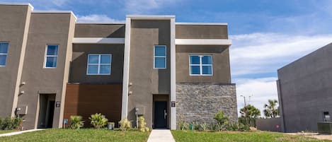 A modern multi-story residential building with a central entrance, a covered garage, and a stone accent wall.
