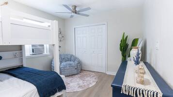 A bedroom with a bunk bed, a ceiling fan, a round rug, a desk with a vase, and a door.