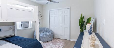 A bedroom with a bunk bed, a ceiling fan, a round rug, a desk with a vase, and a door.