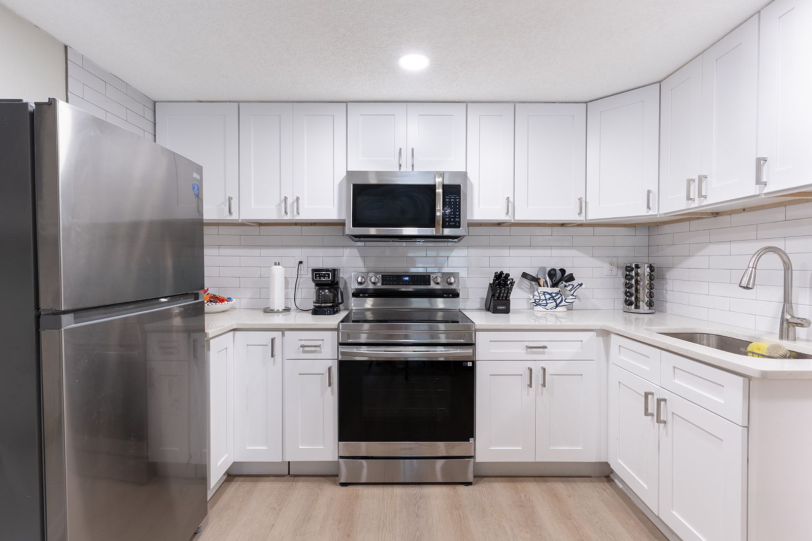A modern kitchen with white cabinets, stainless steel appliances, and a built-in microwave.