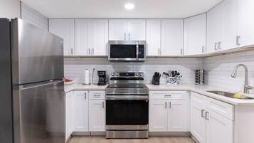 A modern kitchen with white cabinets, stainless steel appliances, and a built-in microwave.