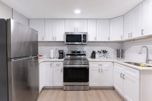 Una cocina moderna con gabinetes blancos, electrodomésticos de acero inoxidable y un microondas integrado.