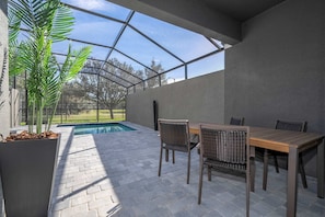 A covered outdoor area with a pool, seating, and a view of the surrounding landscape. - Doppio Westside Home Near Disney with Pool (Kissimmee)