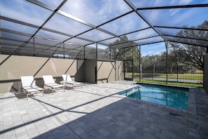 An outdoor pool area with a glass enclosure, lounge chairs, and a view of the surrounding landscape. - Casa Doppio Westside • 4 Bedrooms Disney (Kissimmee)