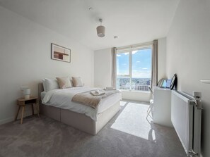 Ein modernes Schlafzimmer mit einem großen Bett, einem Nachttisch, einem Heizkörper und einem Fenster mit Blick auf die Stadt.