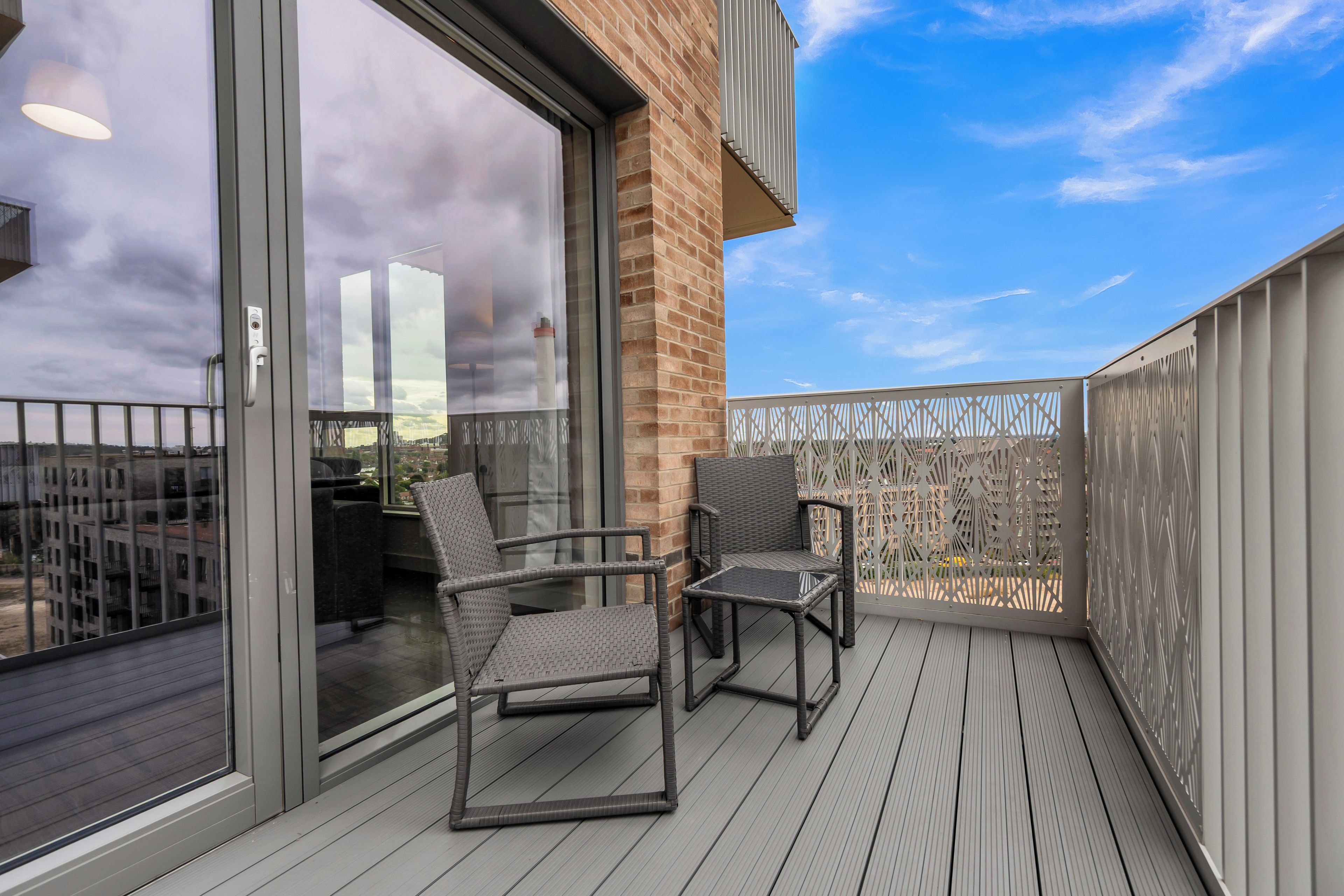 A balcony with two wicker chairs, a glass door, and a view of the cityscape.