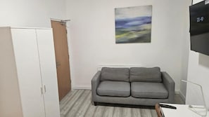 A room with a grey sofa, a white wardrobe, a painting on the wall, and a TV mounted on the wall.