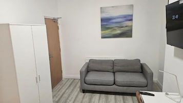 A room with a grey sofa, a white wardrobe, a painting on the wall, and a TV mounted on the wall.