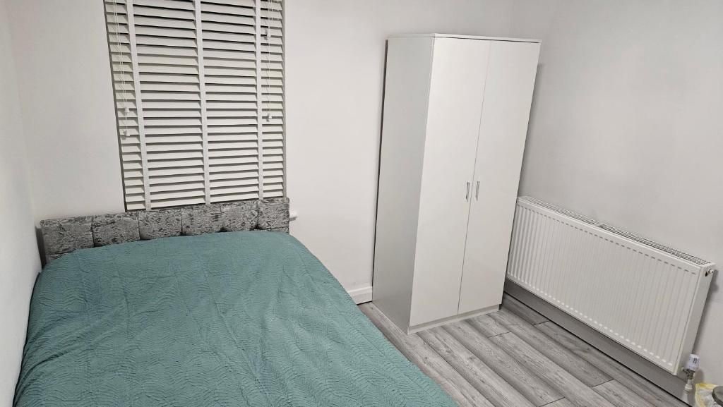 Un dormitorio con cama, armario, radiador y ventana con persianas.