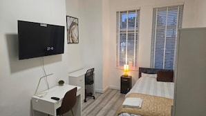 A bedroom with a bed, a desk, a chair, a TV, and a window with blinds. - New Horizon Lodge (LEIGH)