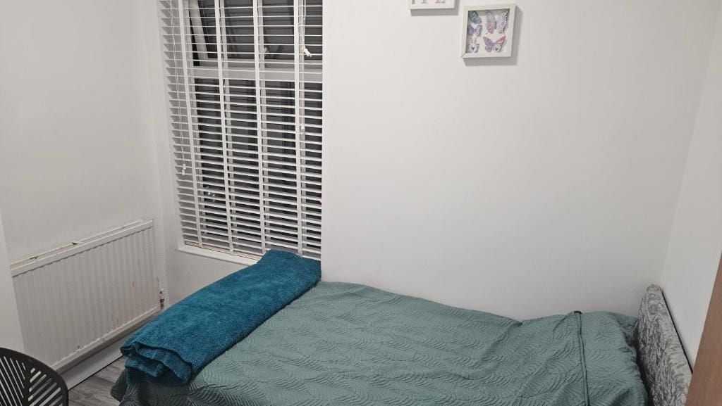 Une petite chambre avec un lit simple, une fenêtre, un radiateur et une serviette bleue sur le lit.