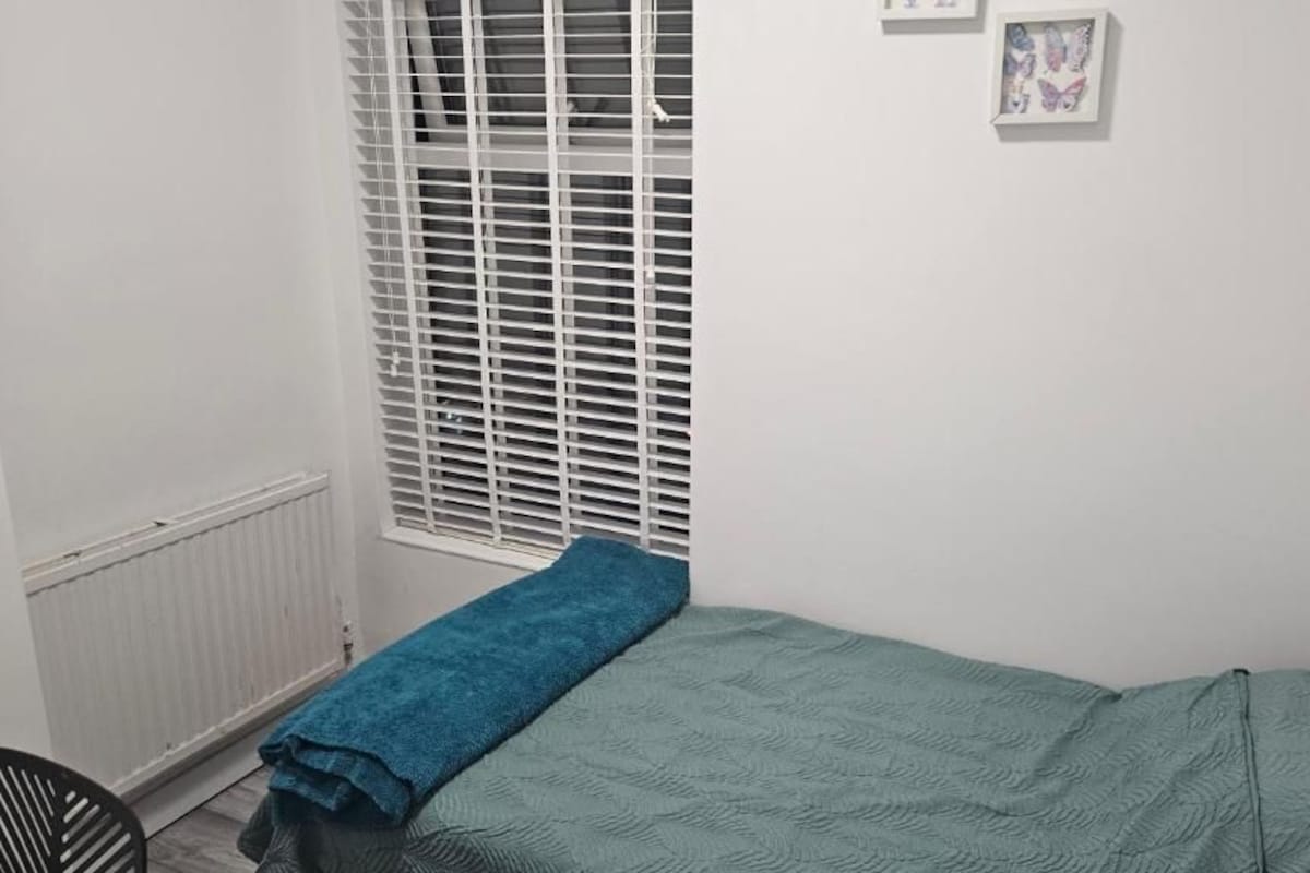 A small, single-bed room with a window, a radiator, and a blue towel on the bed.