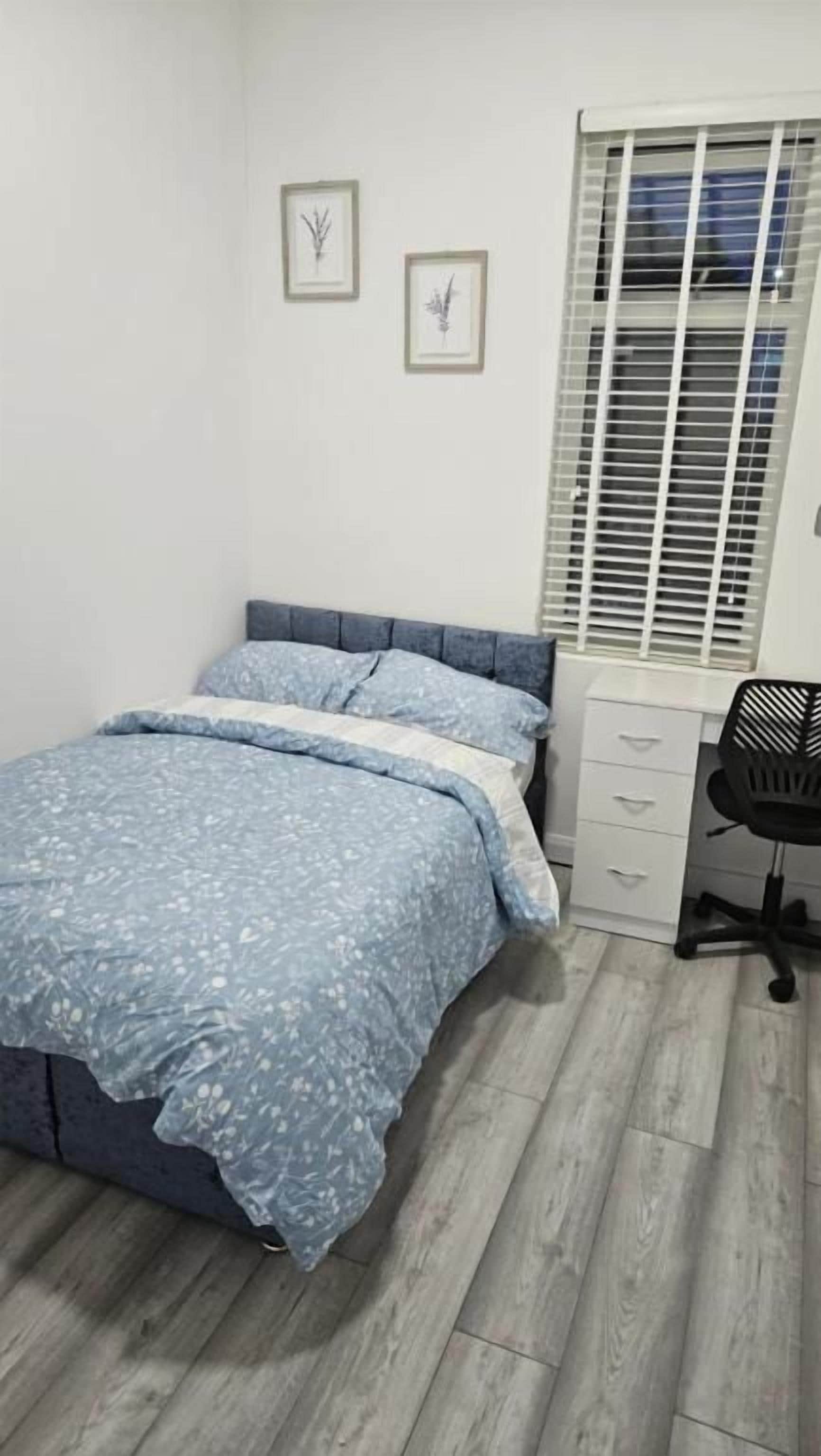 A bedroom with a bed, a desk, and a window with blinds.