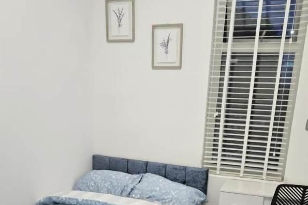 A bedroom with a bed, a desk, and a window with blinds.