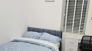 A bedroom with a bed, a desk, and a window with blinds.