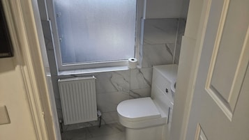 Un baño pequeño con inodoro, un radiador y una ventana.