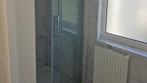 A bathroom with a glass shower enclosure, a window, and a radiator. - New Horizon Lodge (LEIGH)