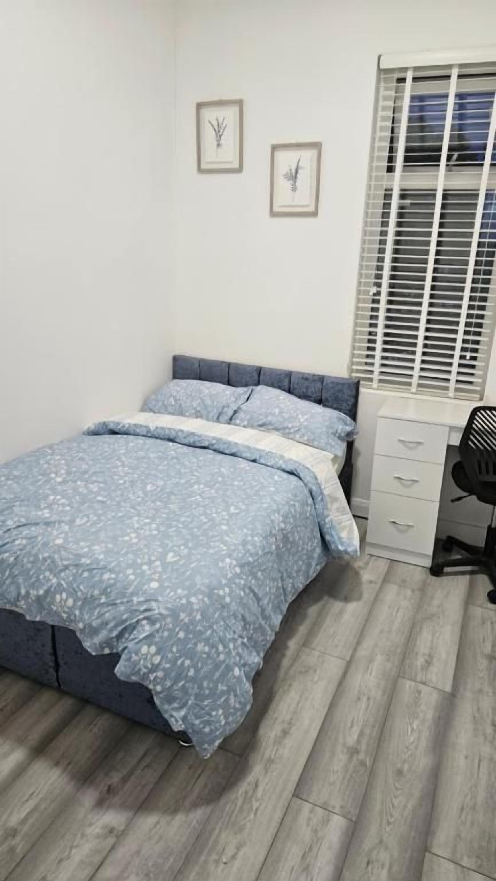 A bedroom with a bed, a desk, and a window with blinds.