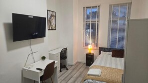Quarto com cama, escrivaninha com cadeira, televisão e janela com persianas.