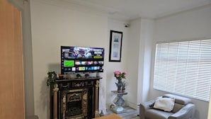 A living room with a fireplace, a television, a sofa, and a window with blinds. - New Horizon Lodge (LEIGH)