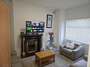 Uma sala de estar com lareira, televisão, sofá e janela com persianas.