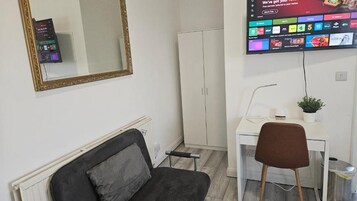 Una habitación con cama, un escritorio con silla, televisor montado en la pared y armario.