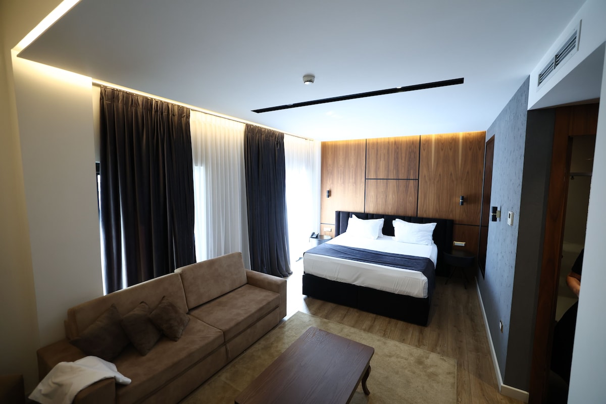 A modern hotel room with a bed, a sofa, a coffee table, and a desk.