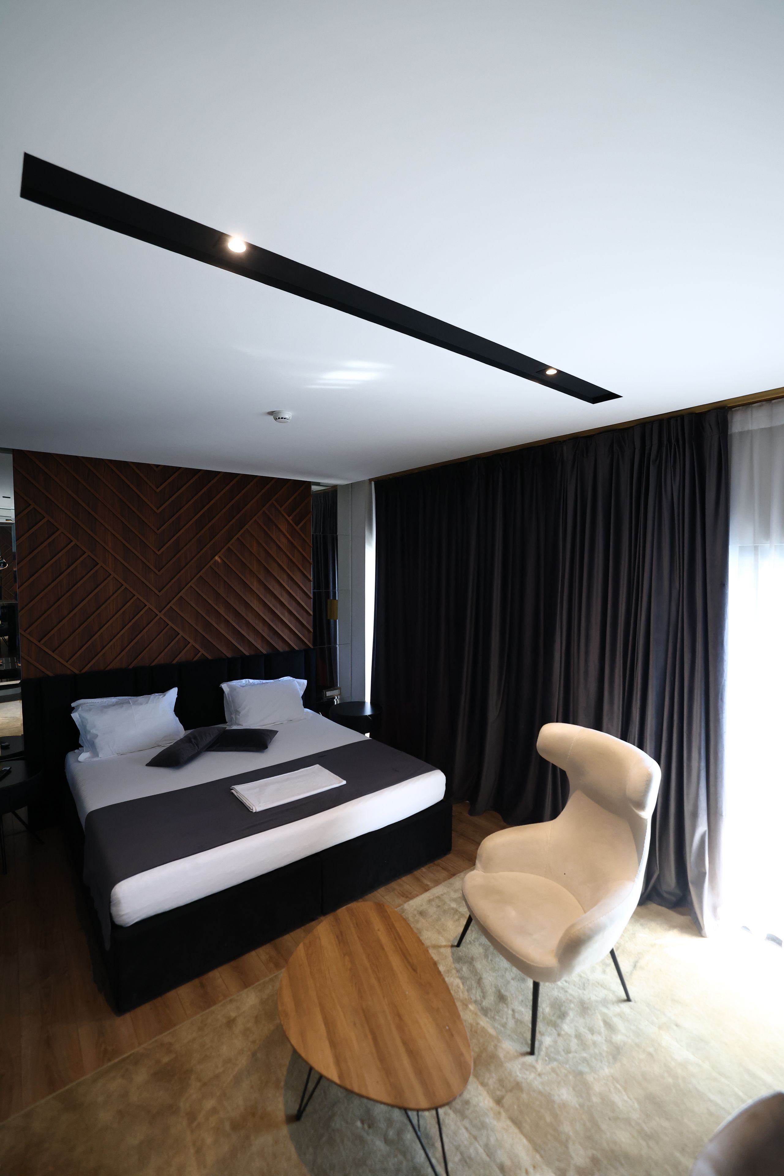 A modern hotel room with a large bed, a bedside table, a chair, and a view of the outdoors.