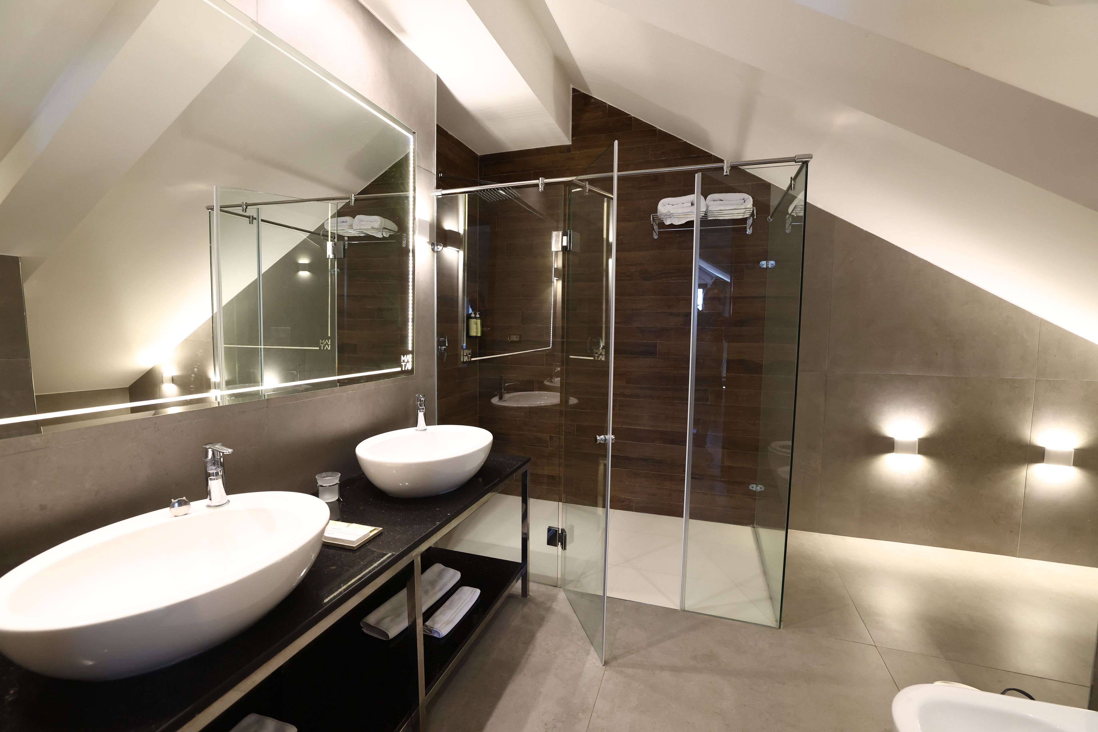 Un baño moderno con ducha de vidrio, dos lavamanos y un espejo grande.