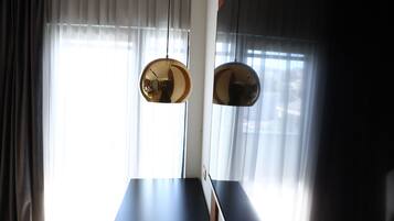 A modern interior with a long dark-colored table, two hanging spherical light fixtures, and a large window with sheer curtains.