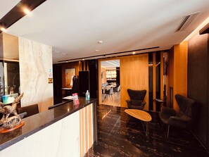 A hotel lobby with a reception desk, seating area, and a dining space.