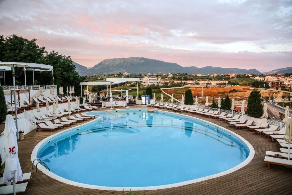 Zona de piscina con sillones de descanso y sombrillas, rodeada por una terraza de madera, con vistas a un paisaje montañoso.