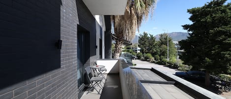 A narrow outdoor corridor with a black tiled wall, a small table with chairs, and a palm tree.