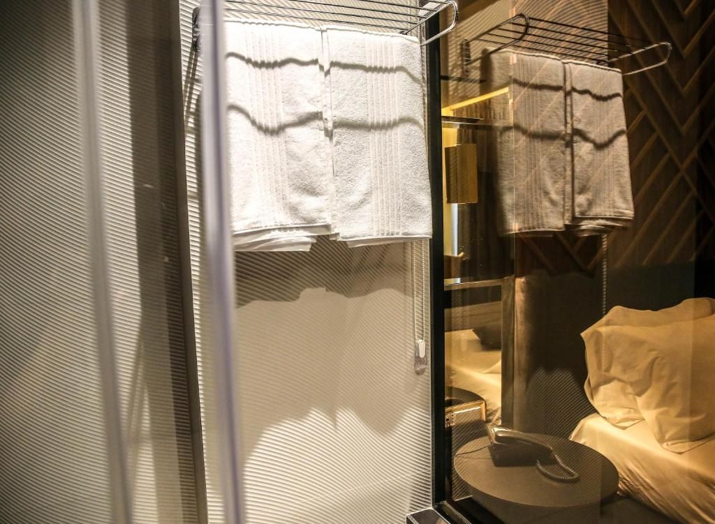 Casa de banho com divisória de vidro, porta-toalhas e cama com cobertura branca.