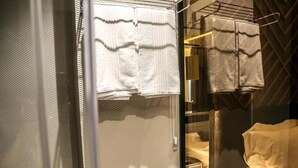 Une salle de bain avec une paroi en verre, un porte-serviettes et un lit recouvert d’une couverture blanche.