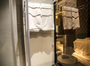 Ein Badezimmer mit Glastrennwand, Handtuchhalter und einem Bett mit weißer Bettdecke.