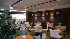 Un espace de détente intérieur moderne, avec des tables et des chaises rondes, un téléviseur à écran plat fixé au mur et une vue sur l’extérieur.
