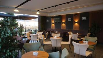 A modern indoor seating area with round tables and chairs, a flat-screen TV mounted on the wall, and a view of the outdoors.