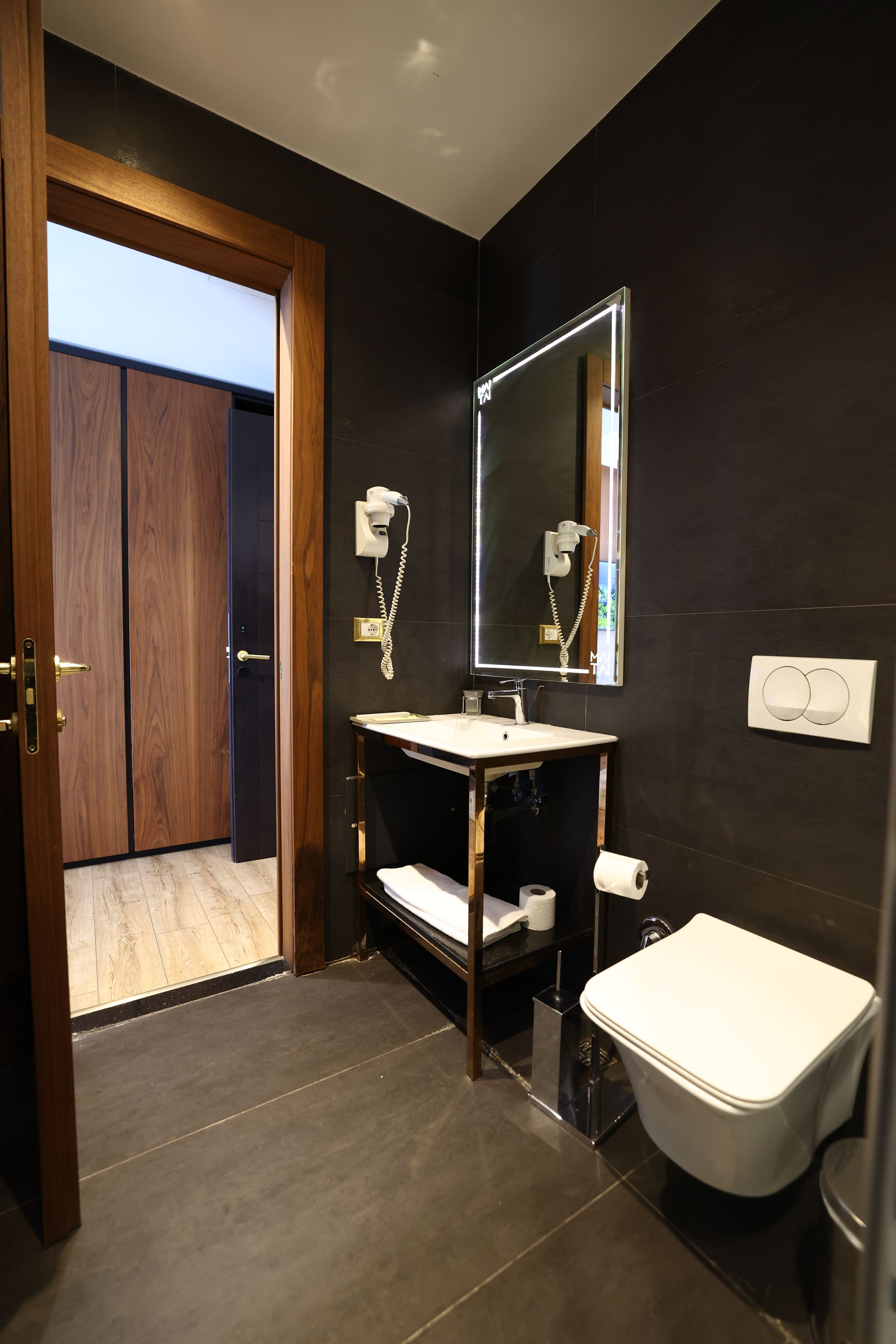Un baño moderno con puerta de madera, lavamanos blanco, espejo y retrete.