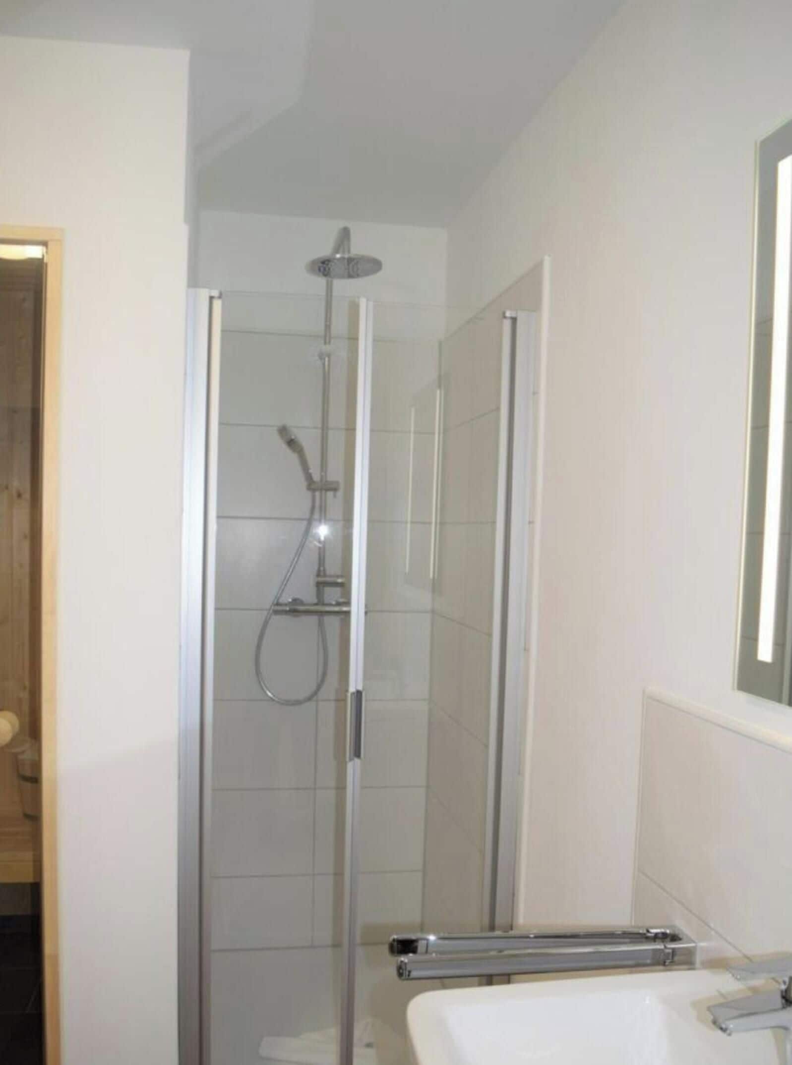 Ein modernes Badezimmer mit einer gläsernen Dusche, einem weißen Waschbecken und einem Spiegel.