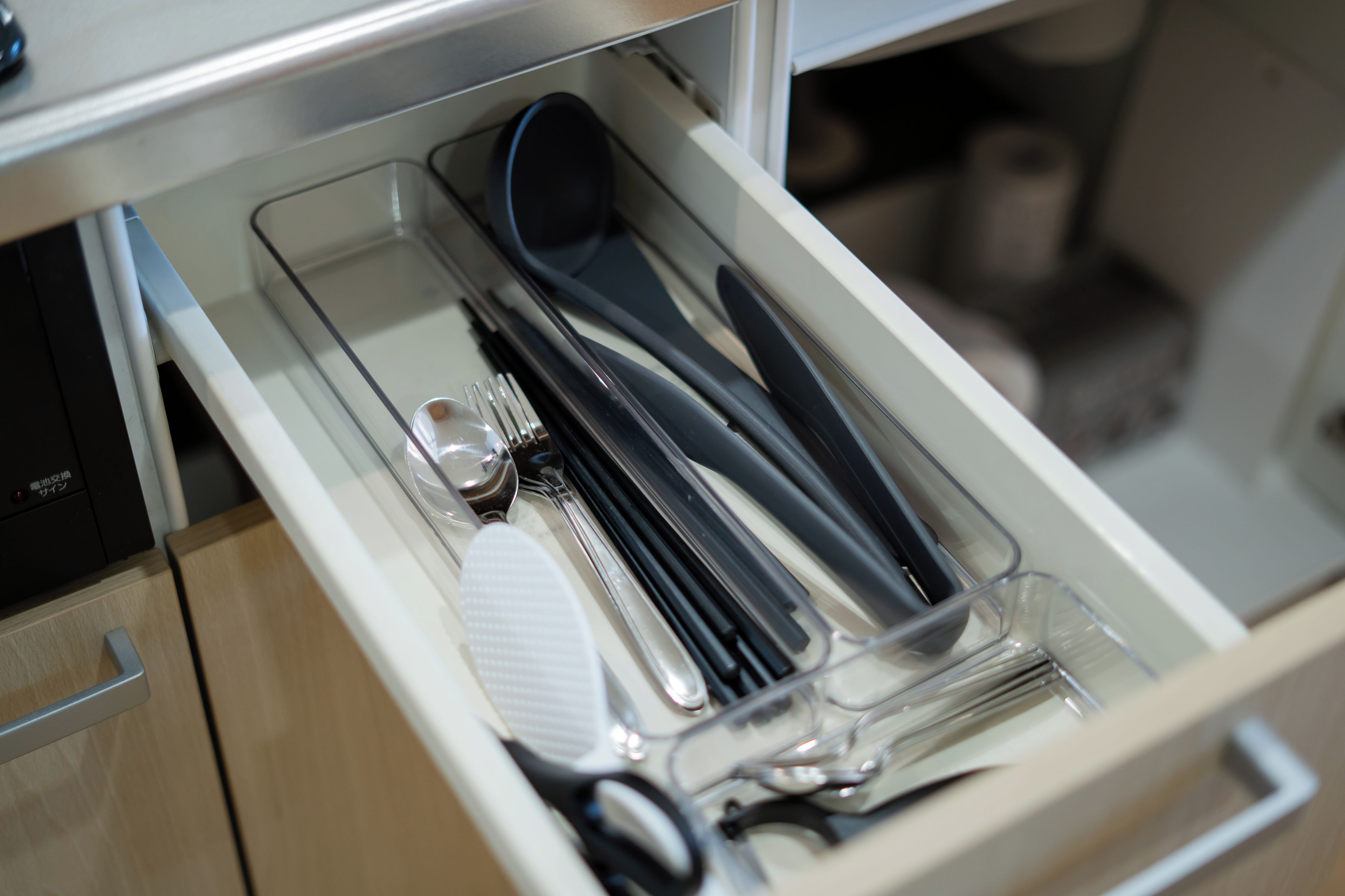 A drawer containing a spoon, fork, knife, and a pair of chopsticks.