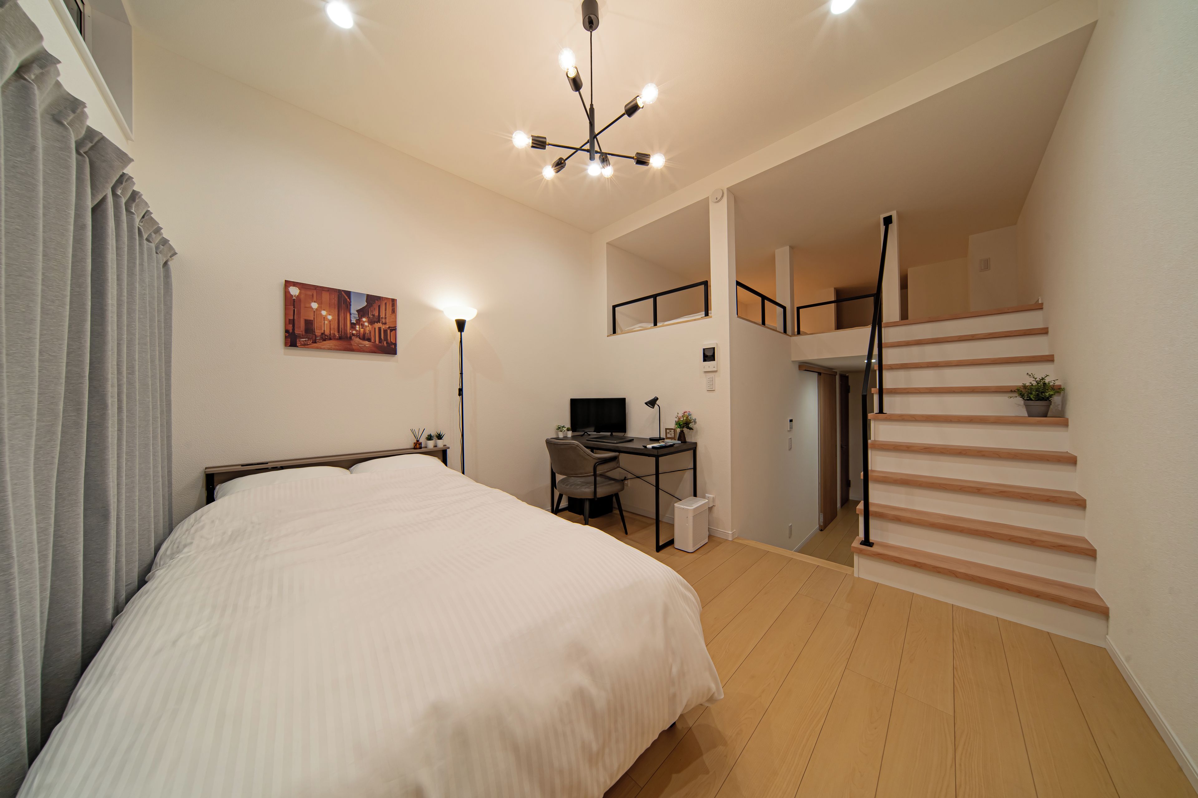 A bedroom with a bed, desk, computer, and a staircase.