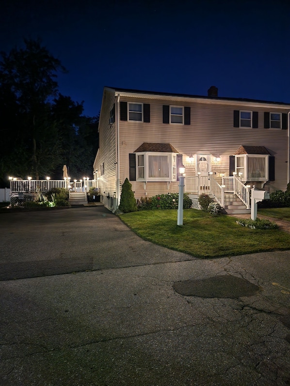 A two-story house with a porch, a small garden, and a driveway. - Quiet 3BR Haven ~ Sleeps 8, Deck, 2 Parking Spots (Lawrence)