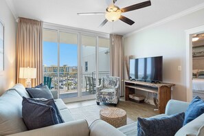 A modern living room with a large flat-screen TV, a ceiling fan, and a balcony with a view of the city. - Beachfront Bliss at Fort Walton Beach (Fort Walton Beach)