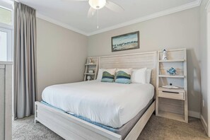 Een slaapkamer met een enkel bed, een nachtkastje, een kaptafel, een plafondventilator en een schilderij aan de muur.