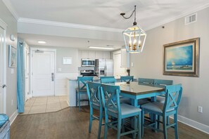 A dining area with a table and chairs, a kitchen in the background, and a painting on the wall. - Beachfront Bliss at Fort Walton Beach (Fort Walton Beach)