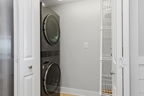 A laundry room with two stacked front-loading washers and dryers, a white door, and a metal rack on the wall. - Beachfront Bliss at Fort Walton Beach (Fort Walton Beach)