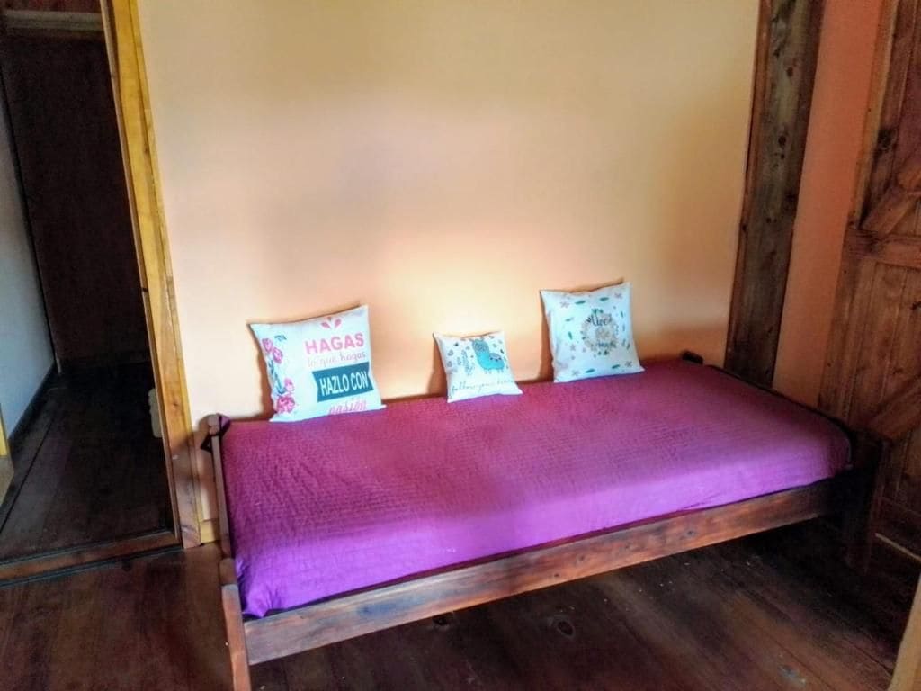 A single bed with a purple bedspread and three pillows with text.