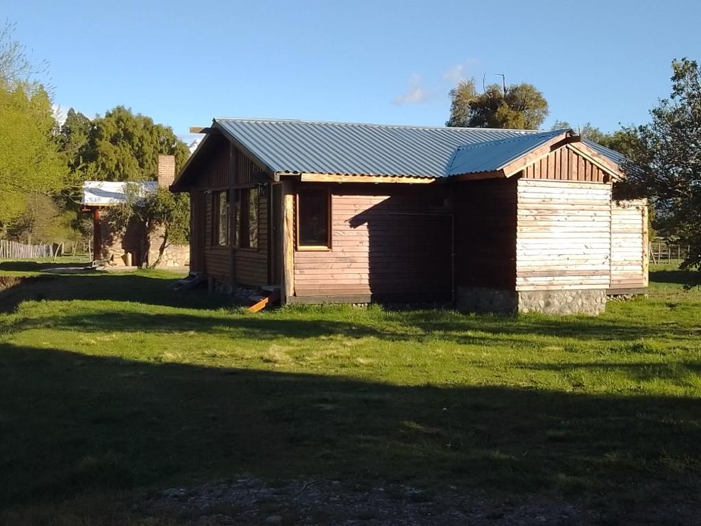 A small wooden structure with a metal roof, likely a shed or storage building, situated in a grassy area with trees in the background.